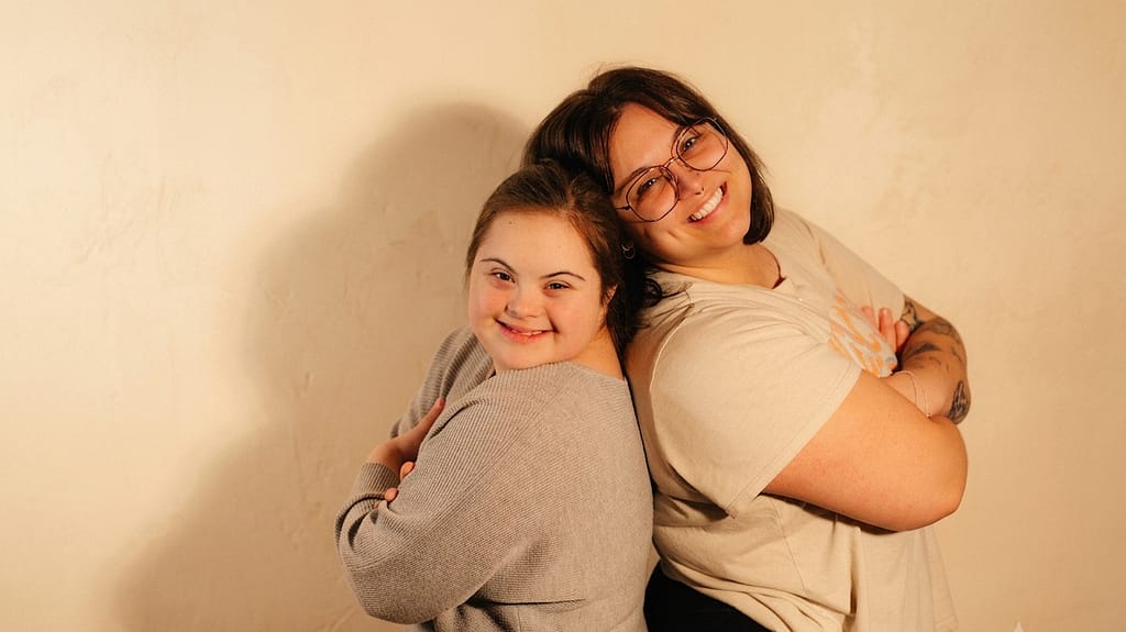 Two young women smile back to back, one with Down syndrome, in a warm portrait representing special needs guardian duties in Indiana